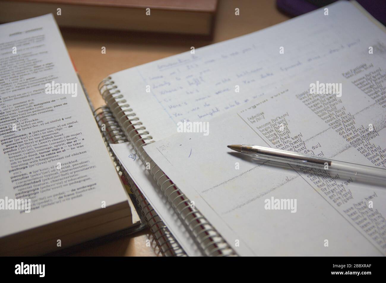 Alcuni notebook, insieme a un dizionario spagnolo inglese sul tavolo di uno studente di lingua inglese Foto Stock