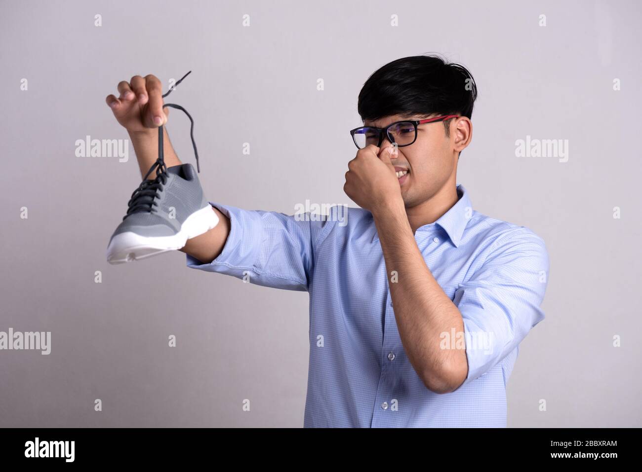 Primo piano l'uomo asiatico che tiene la scarpa sporca e puzzolente con un'espressione di disgusto. Concetto di assistenza sanitaria. Foto Stock