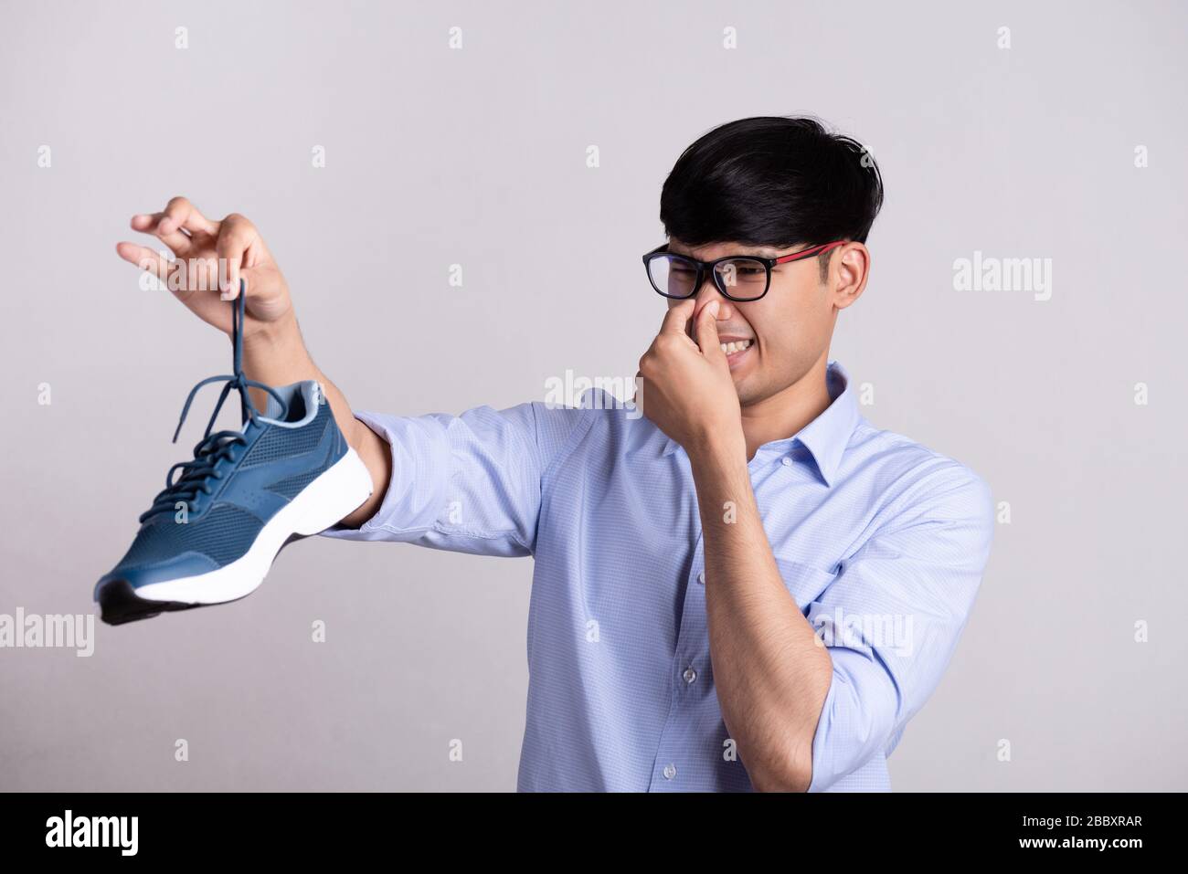 Primo piano l'uomo asiatico che tiene la scarpa sporca e puzzolente con un'espressione di disgusto. Concetto di assistenza sanitaria. Foto Stock