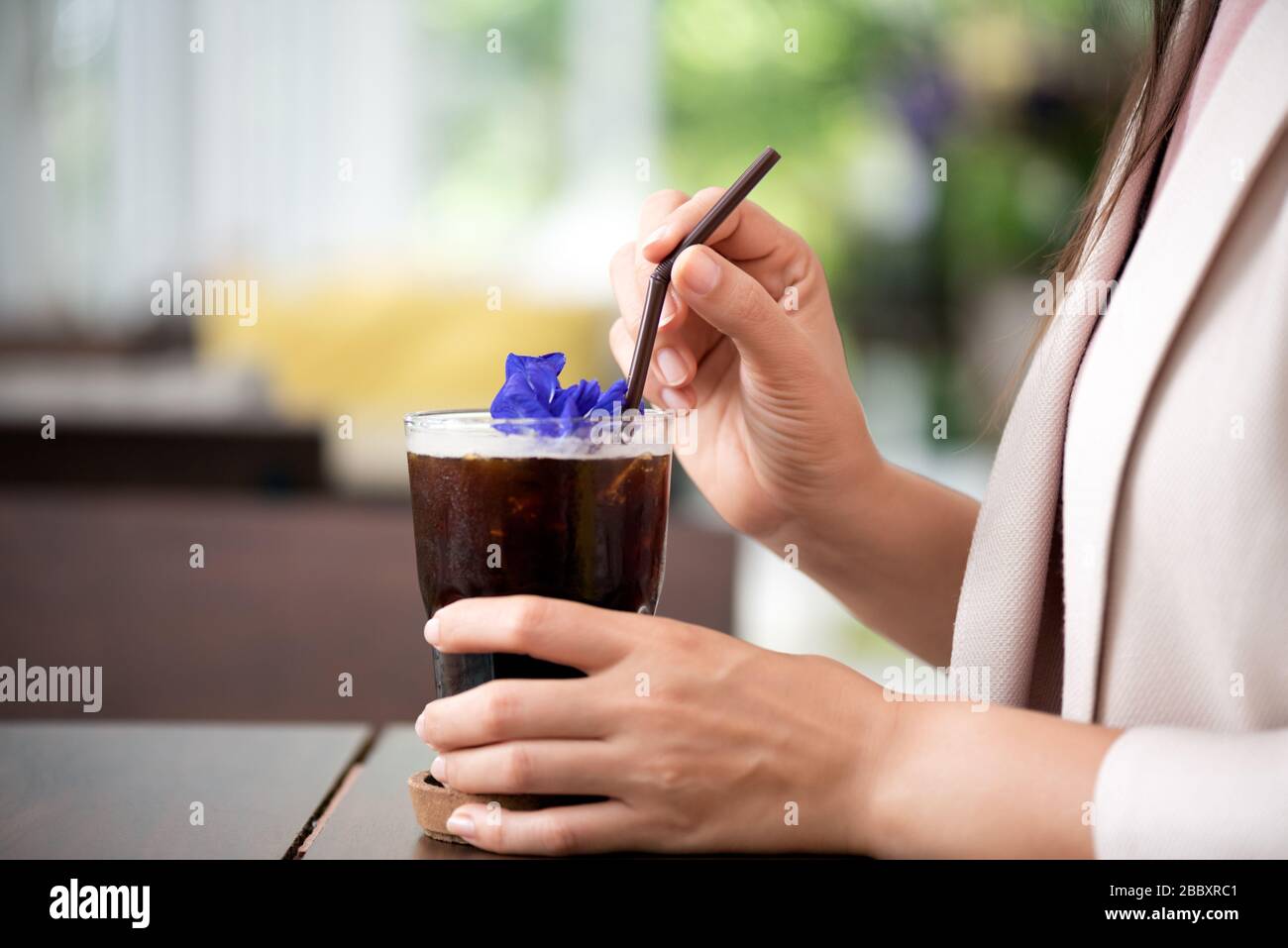 Closeup di donna mano tenendo la paglia con una bevanda caffè freddo con fiori di pisello farfalla. Foto Stock