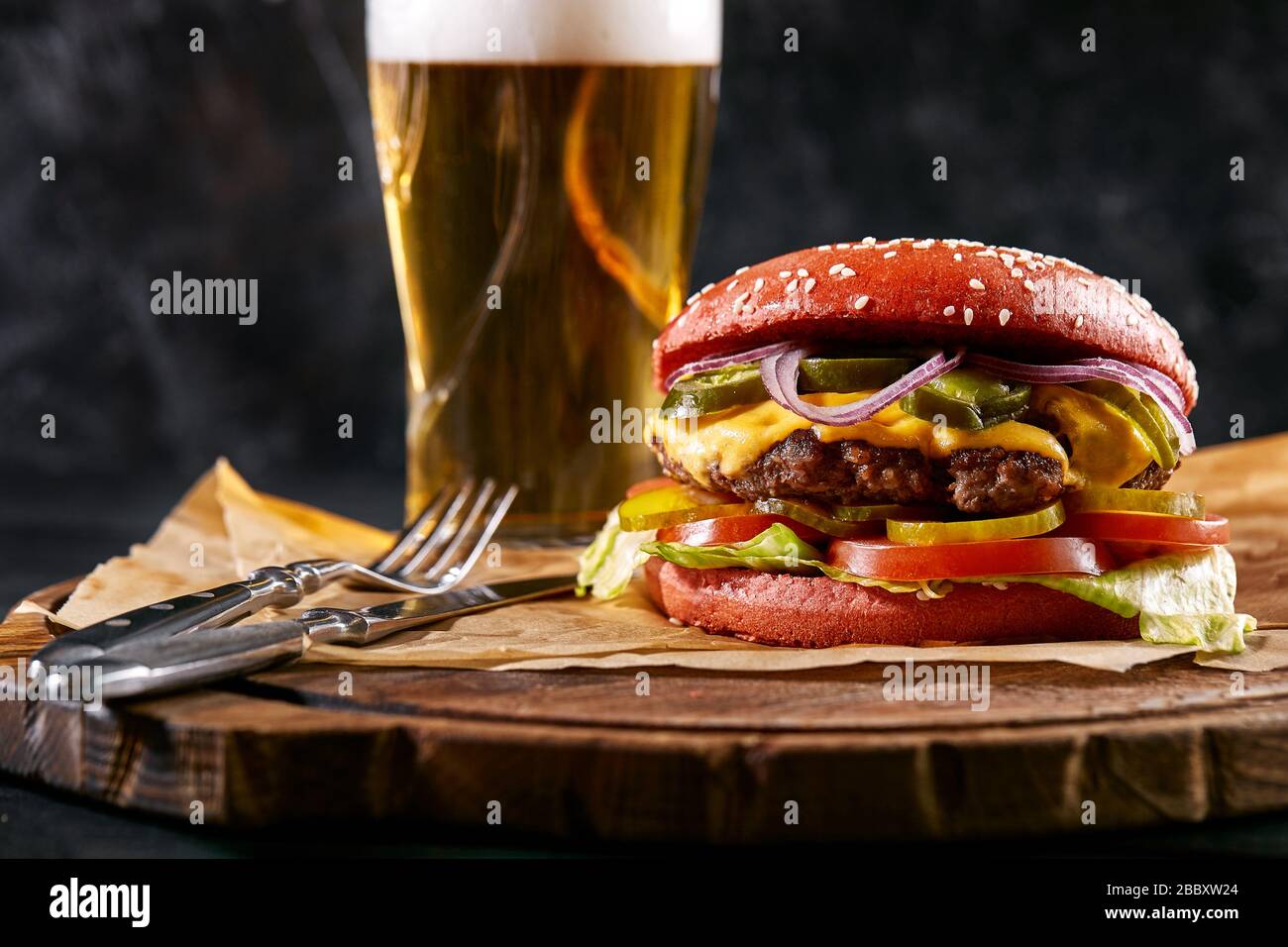 Hamburger succulento, patatine fritte, salse e un bicchiere di birra fredda su sfondo di legno scuro. Copia spazio, fast food set, foto del cibo Foto Stock