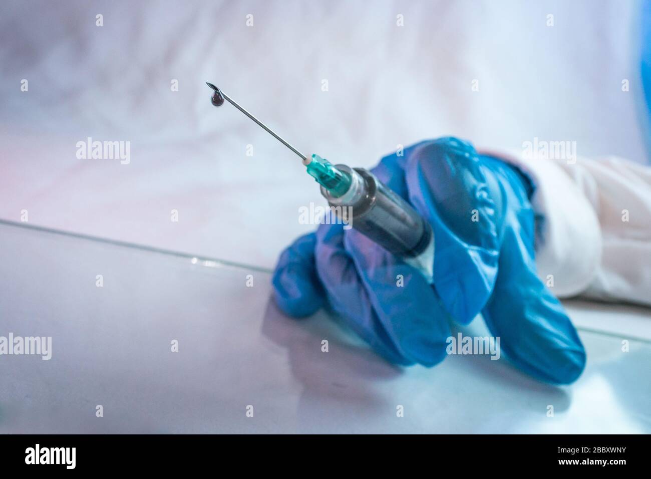 goccia di vaccino in siringa per il trattamento di covid 19 con l'uso di guanti blu 10 Foto Stock