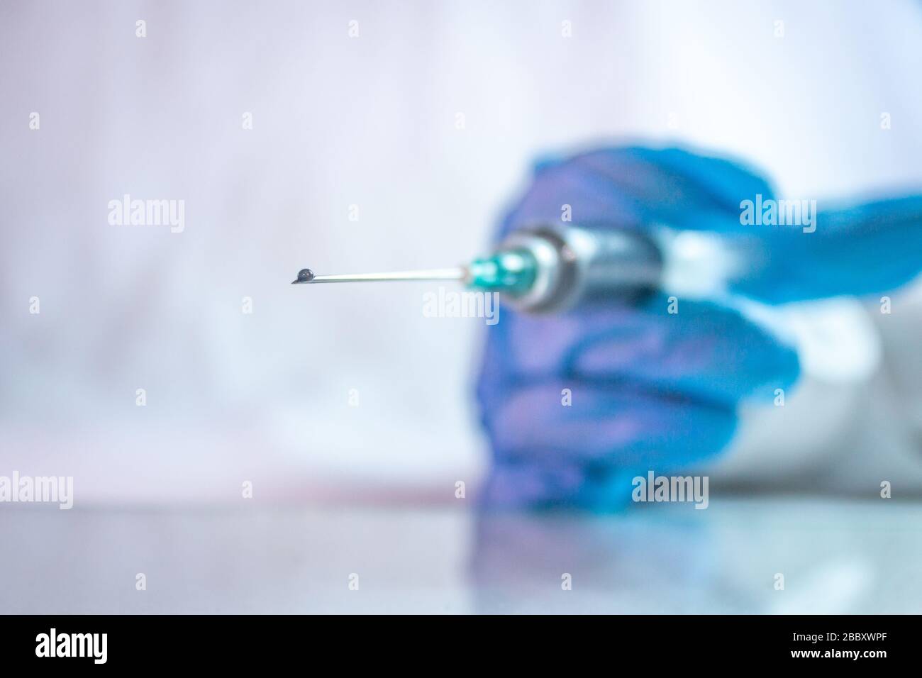 goccia di vaccino in siringa per il trattamento di covid 19 con l'uso di guanti blu Foto Stock