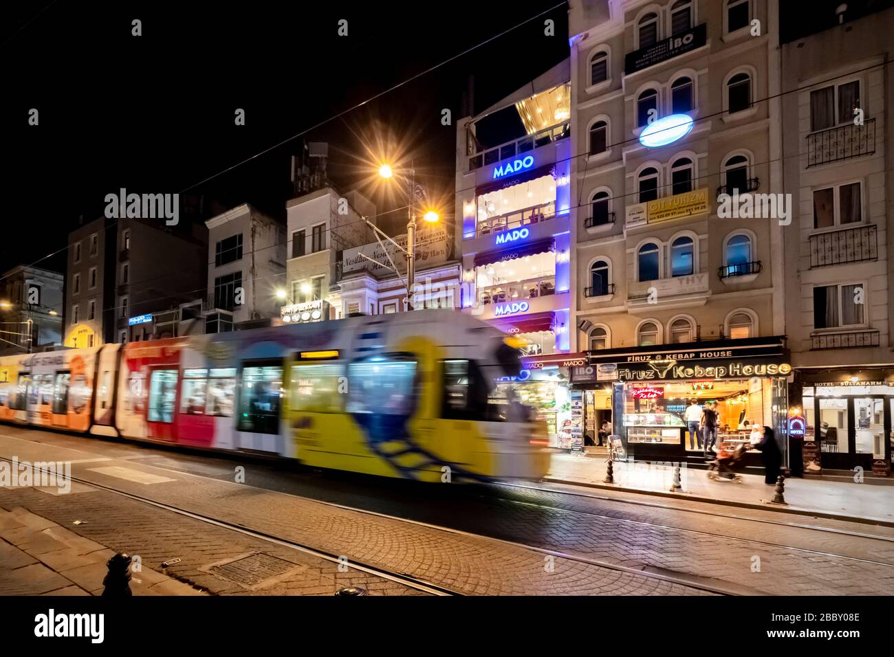 Un tram è sfocato come si accelera attraverso la strada, oltre caffè e negozi vicino alla Moschea Blu nel quartiere Sultanahmet di Istanbul, turchia di notte. Foto Stock