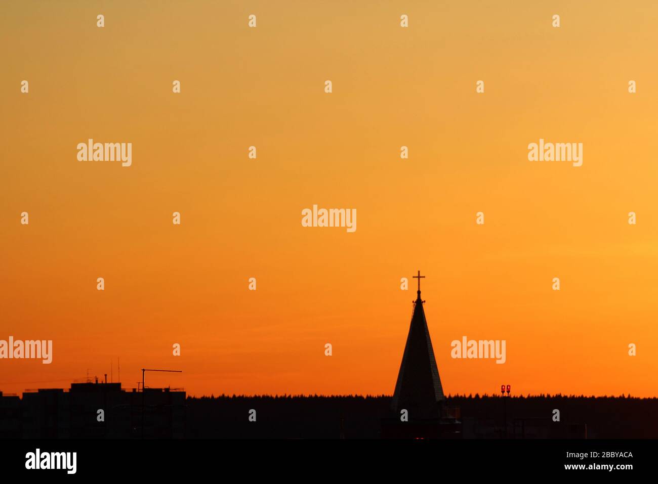 Sole sotto l'orizzonte e il tetto della chiesa con una croce sullo sfondo ardente cielo arancione drammatico al tramonto o all'alba retroilluminata dal sole. Luogo per il testo e il disegno. Foto Stock