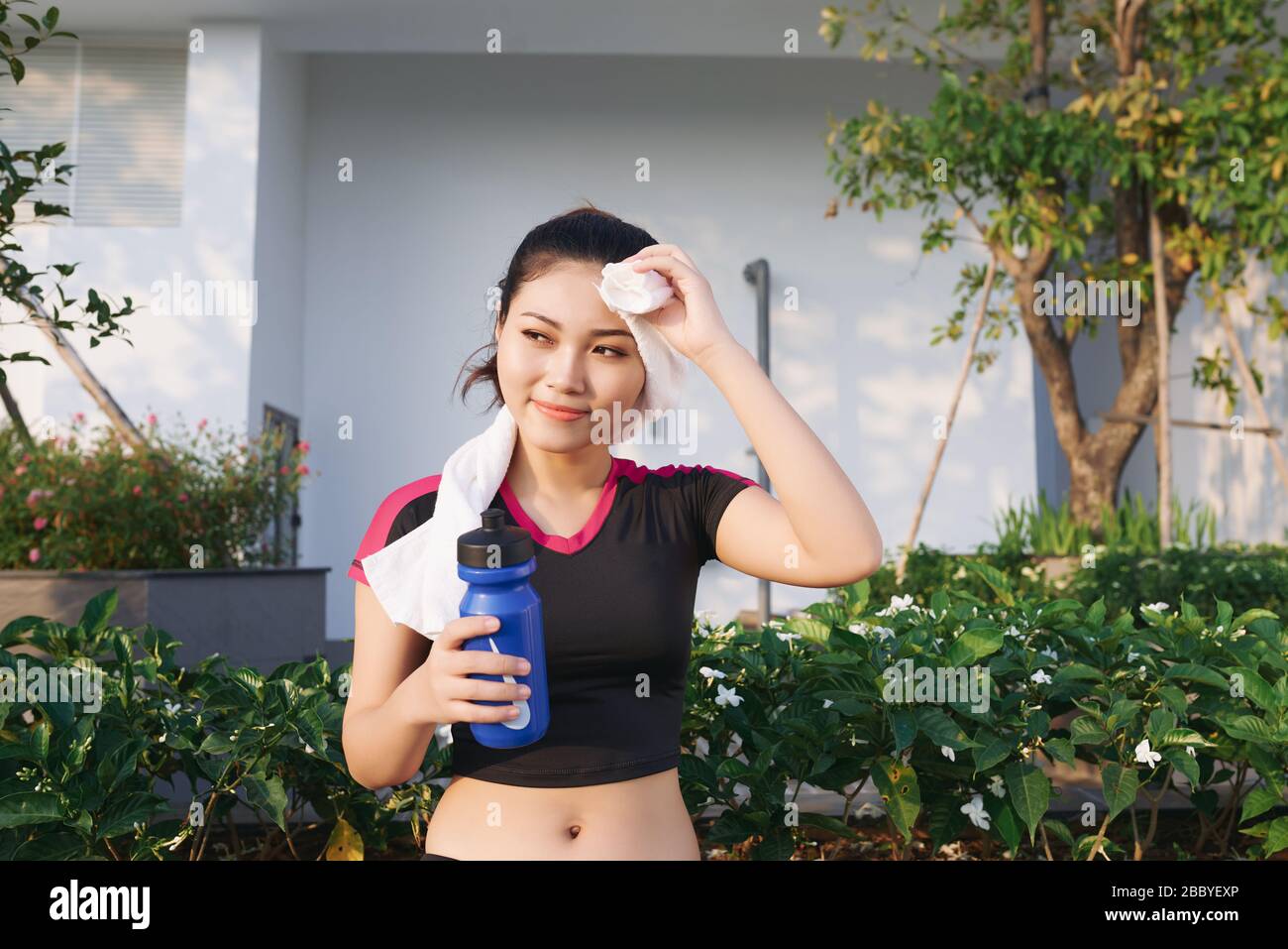 Stunning fitness donna asiatica strofinare sudore e tenere una bottiglia d'acqua dopo jogging o corsa all'aperto Foto Stock