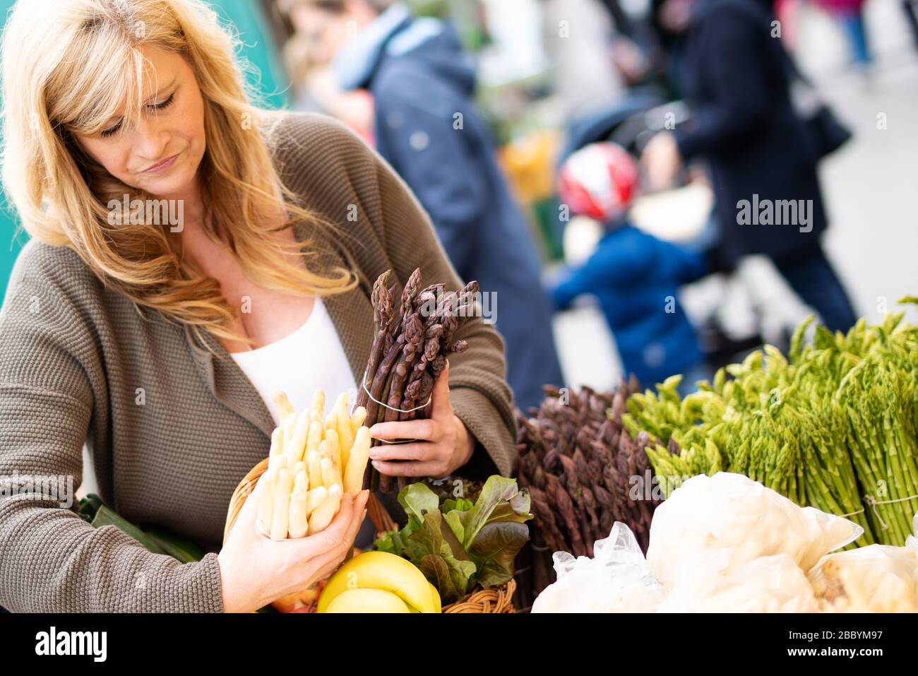 Una donna di mezza età acquista asparagi in un mercato settimanale, la stagione degli asparagi Foto Stock