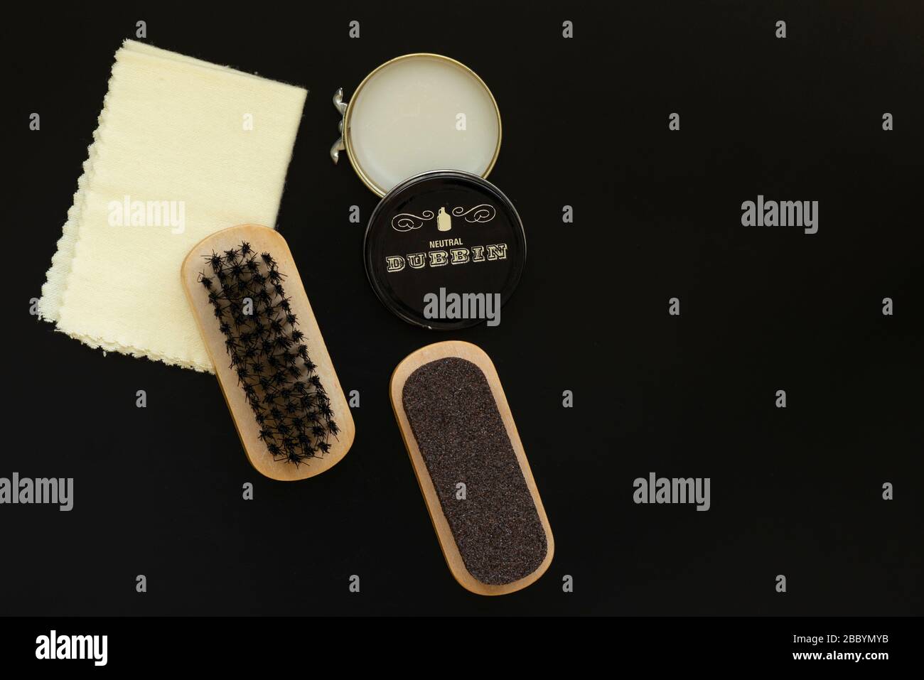 Spazzola, panno morbido, pasta di cera dubbin e carta vetrata ruvida come kit per la cura del bagagliaio vintage o accessori per kit lustrascarpe su sfondo nero dall'alto. Foto Stock