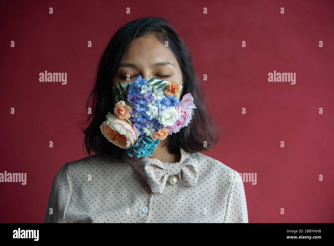 Donna in maschera medica protettiva con fiori su sfondo rosso. Protezione Covid -19. Foto Stock