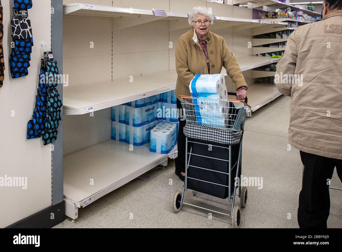 Signora anziana in supermercato con grande pacco di rotolo di servizi igienici nel suo carrello durante l'acquisto di panico di Coronavirus nel Regno Unito marzo 2020 Foto Stock