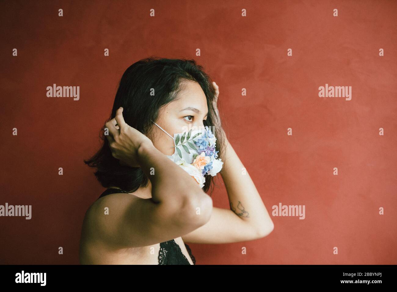 Donna in maschera medica protettiva con fiori su sfondo rosso. Protezione Covid -19. Stile retrò Foto Stock