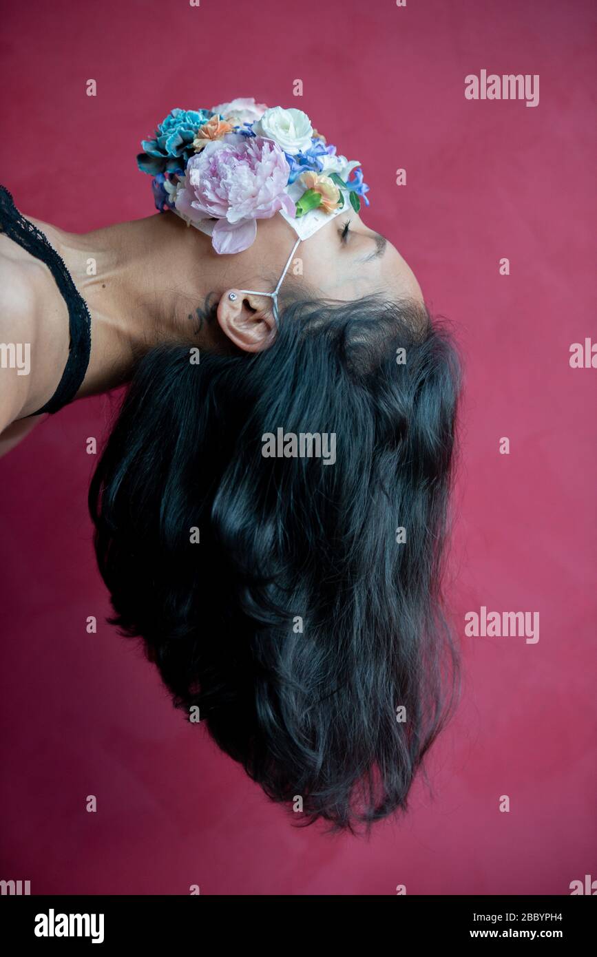 Donna in maschera medica protettiva con fiori su sfondo rosso. Protezione Covid -19. Foto Stock