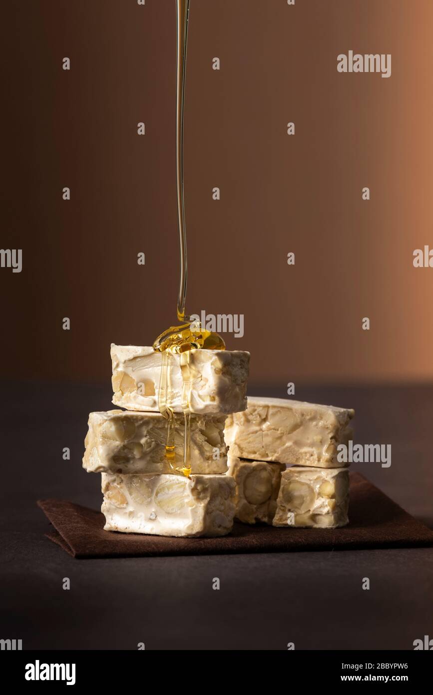 piccoli pezzi di torrone su tavolo scuro con miele gocciolante Foto Stock