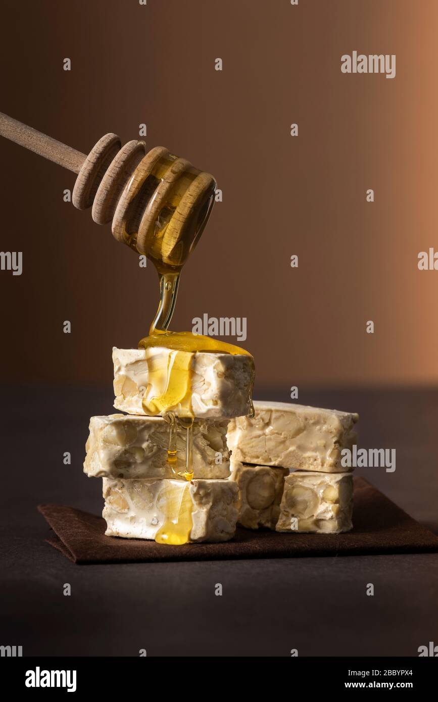 piccoli pezzi di torrone su tavolo scuro con miele gocciolante Foto Stock