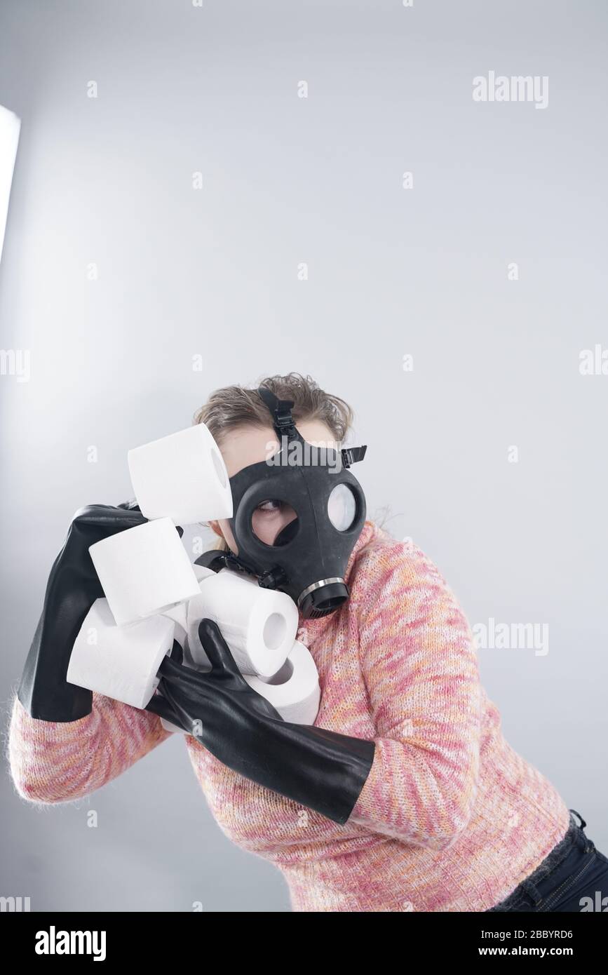donna spaventata in una maschera di gas e guanti prende tutta la carta igienica dal negozio durante la coronovirus covid epidemia. Foto Stock