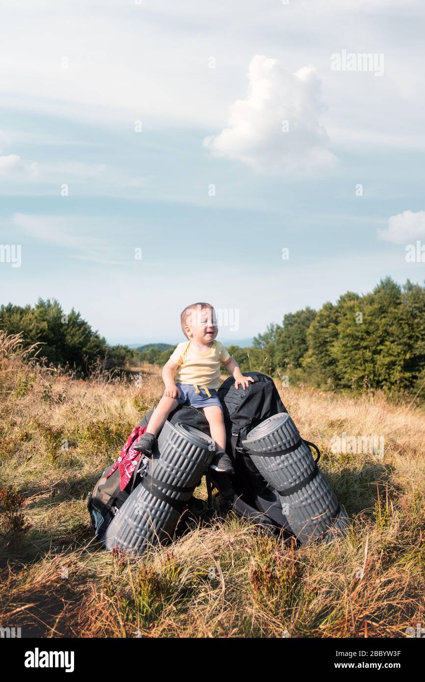 Piccolo bambino seduto sui zaini turistici in autunno montagne. Concetto di viaggio Foto Stock