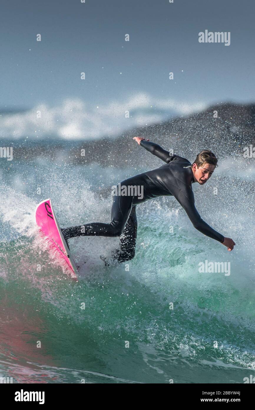 Spettacolare surf azione come un giovane surfista maschio cavalcare un onda a Fistral a Newquay in Cornovaglia. Foto Stock