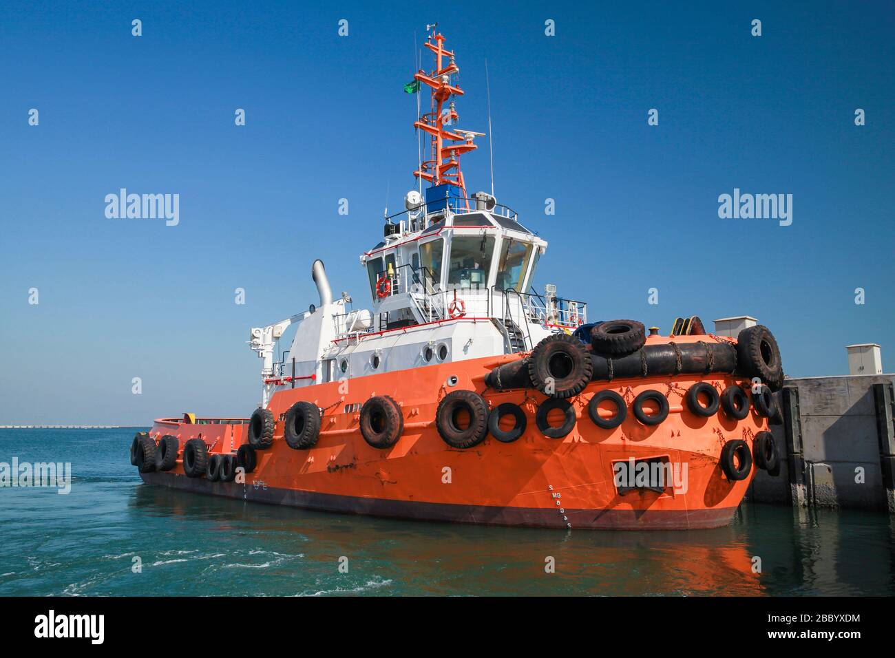 Rimorchiatore con scafo arancione brillante è ormeggiato in un porto Foto Stock