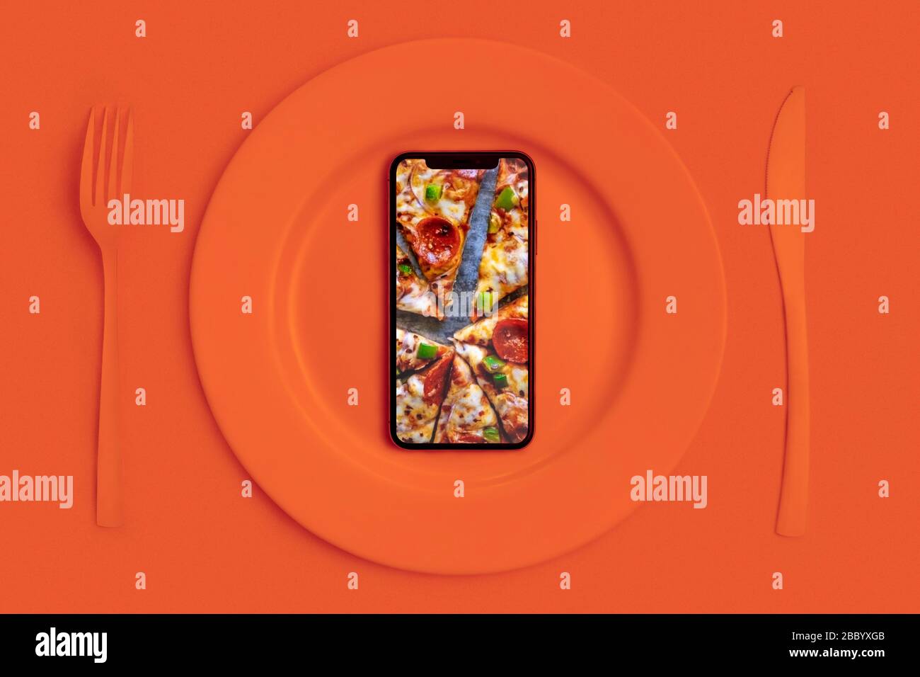 Ordinare cibo online, consegna cibo. Chiama e porta il cibo a casa. Smartphone con pizza sullo schermo, appoggiato su un piatto, un coltello e una forcella. Arancione. La vista Foto Stock