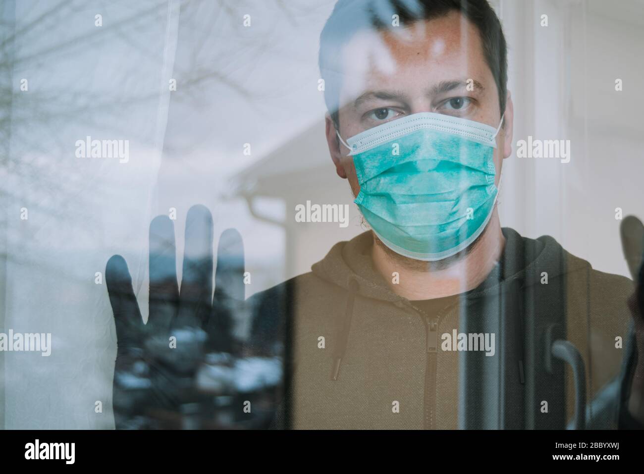 uomo in quarantena guardando finestra trogolo con maschera e guanti in isolamento proteggere da coronavirus covid-19 Foto Stock