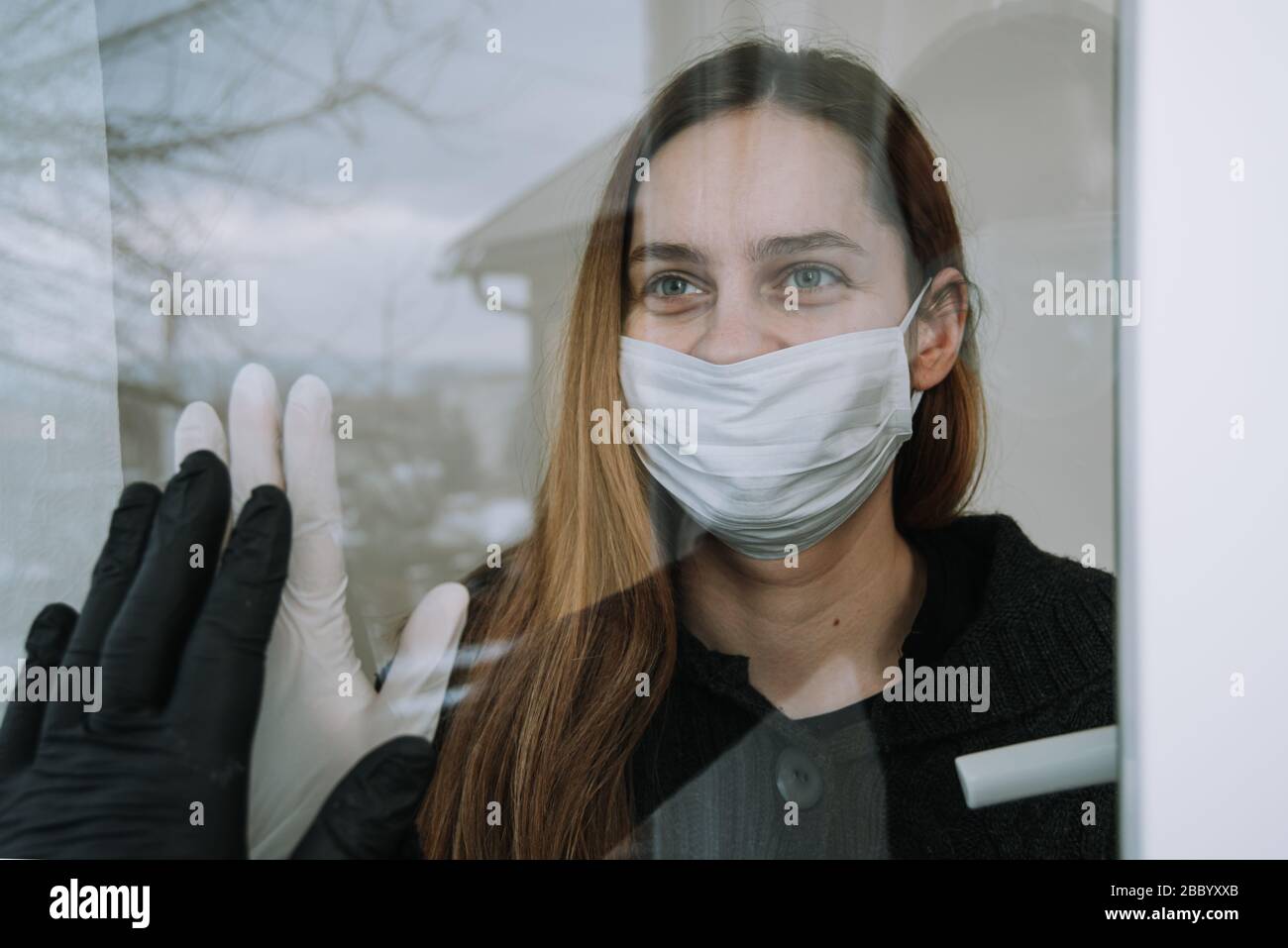 donna in quarantena vedendo il suo fritto che è venuto a visitarla a causa di coronavirus covid-19 maschera di spirito e guanti sulla finestra a casa Foto Stock