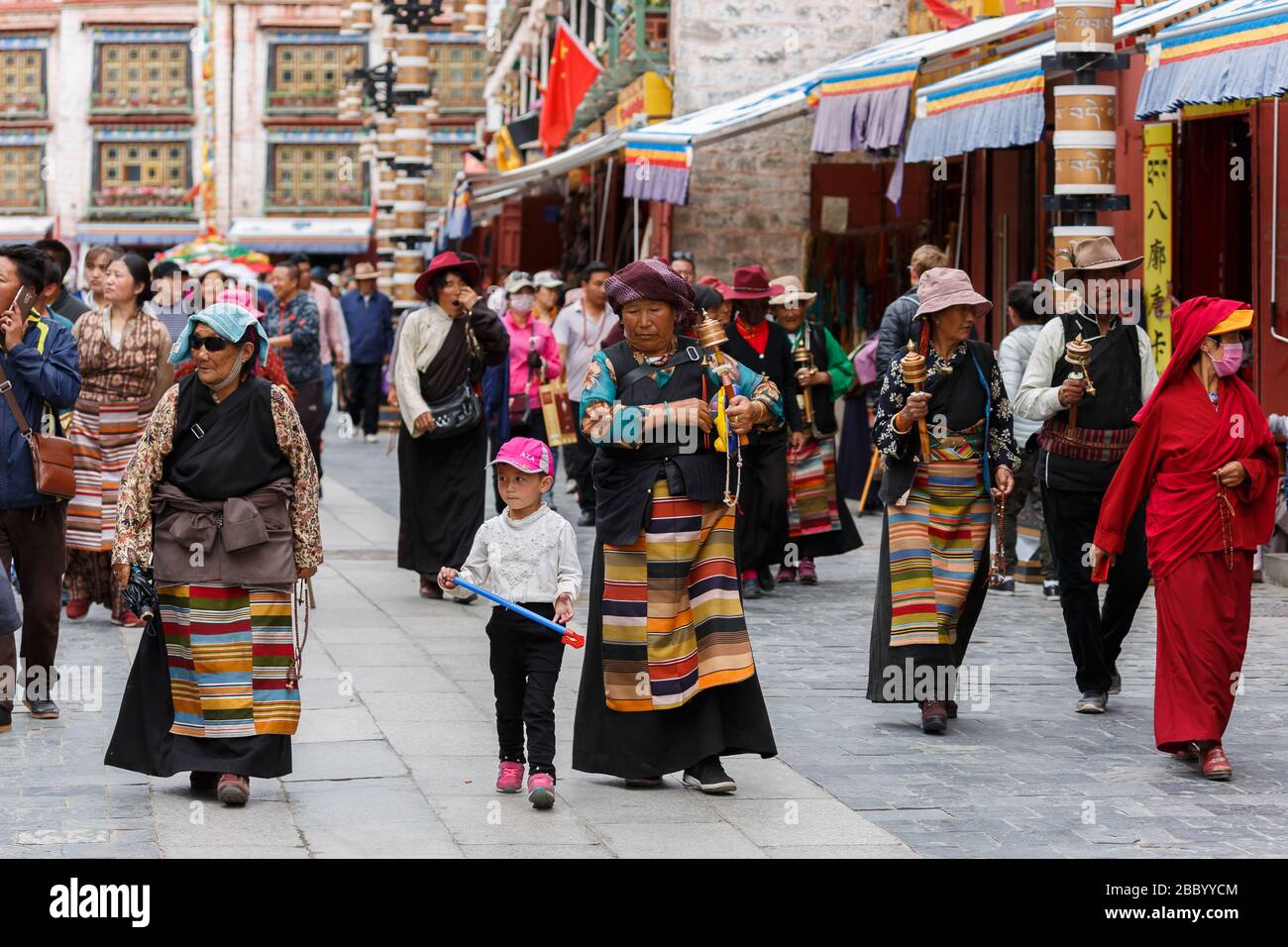 Un gruppo di pellegrini tibetani che camminano in via Barkhor. Stanno tenendo perline di preghiera e ruote di preghiera delle mani. Passeggiate in cerchio intorno al tempio di Jokhang. Foto Stock