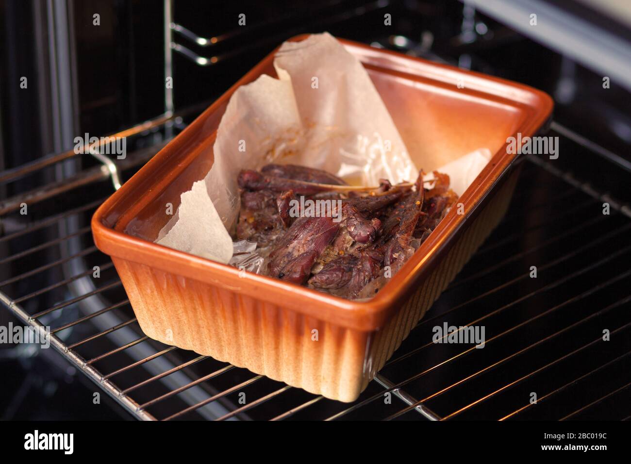 La carne di anatra viene cotta nel forno su un foglio di cottura in ceramica. Foto ravvicinata. Foto Stock