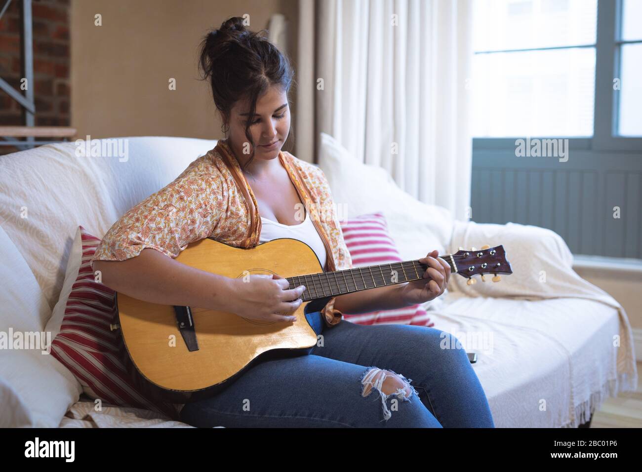 Più dimensione femminile vlogger auto isolamento suonare la chitarra a casa Foto Stock