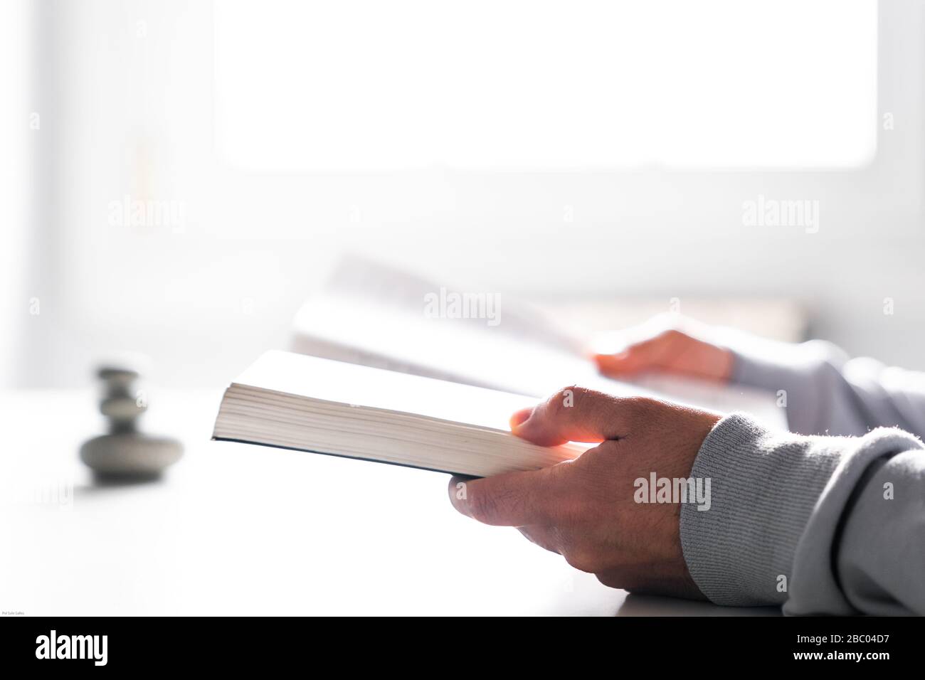 Leggere un libro con la luce bianca dalla finestra. Tenere un libro in entrambe le mani. Foto Stock