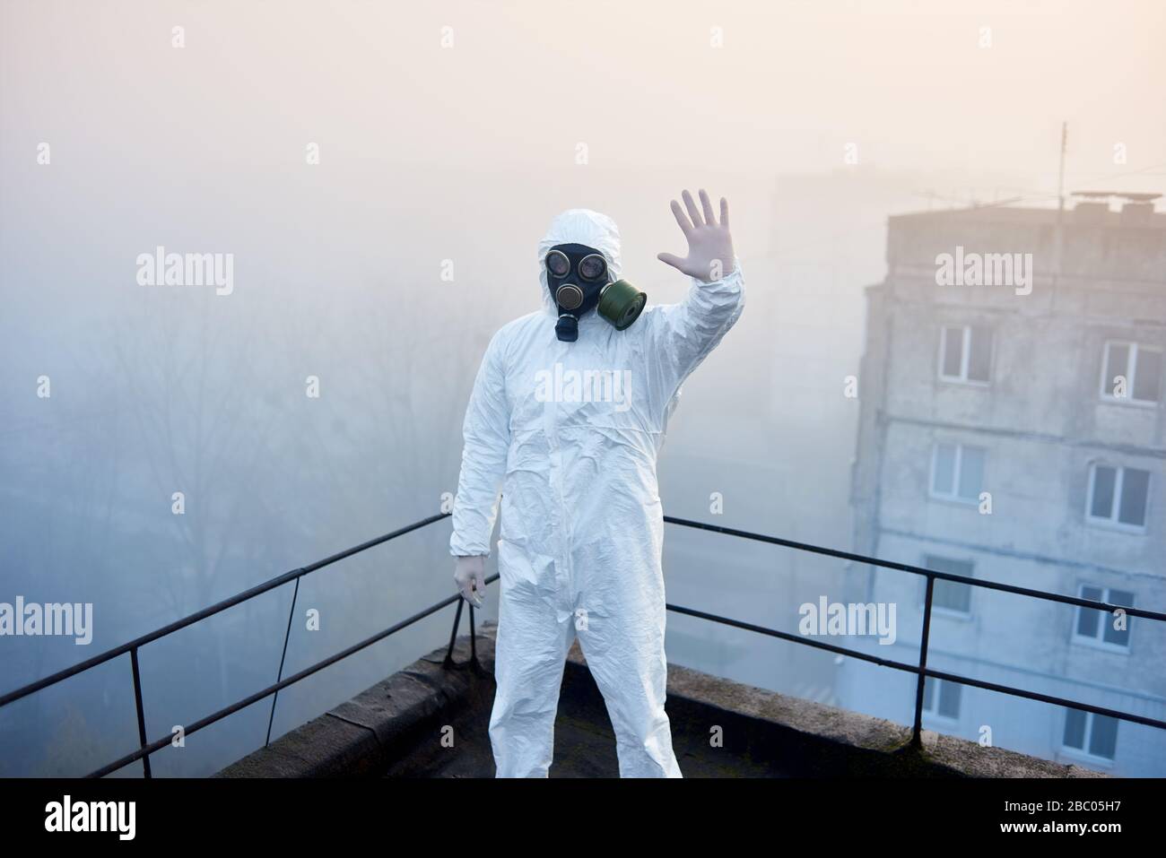 Uomo in vestito protettivo, mostrando segno di stop è al centro della fotografia istantanea sul tetto in caso di nebbia meteo, facendo la ricerca sull'inquinamento ambientale Foto Stock