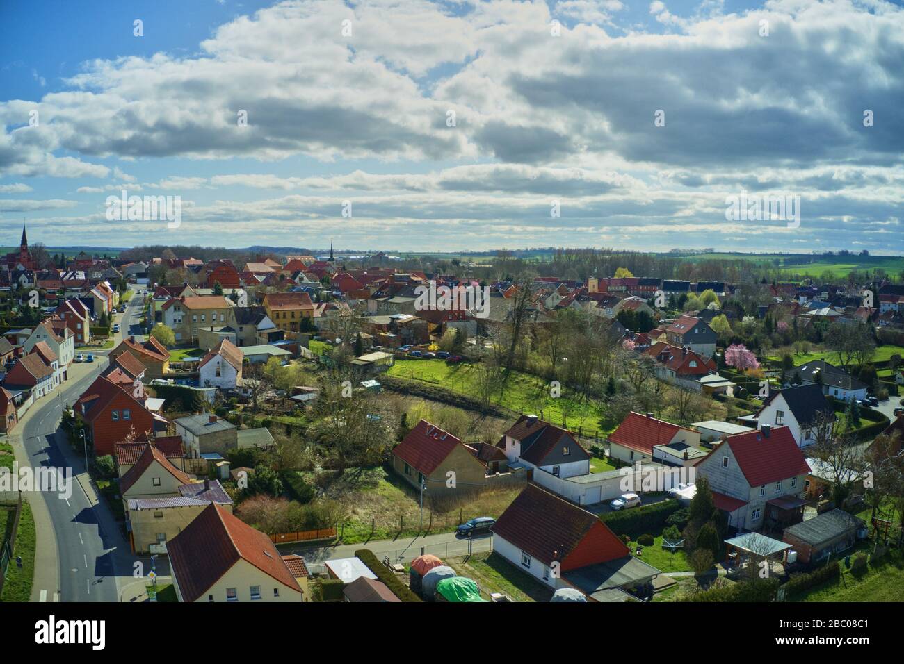 Veduta aerea di un villaggio in Germania, sotto il sole luminoso, con cielo nuvoloso e molti giardini e prati Foto Stock