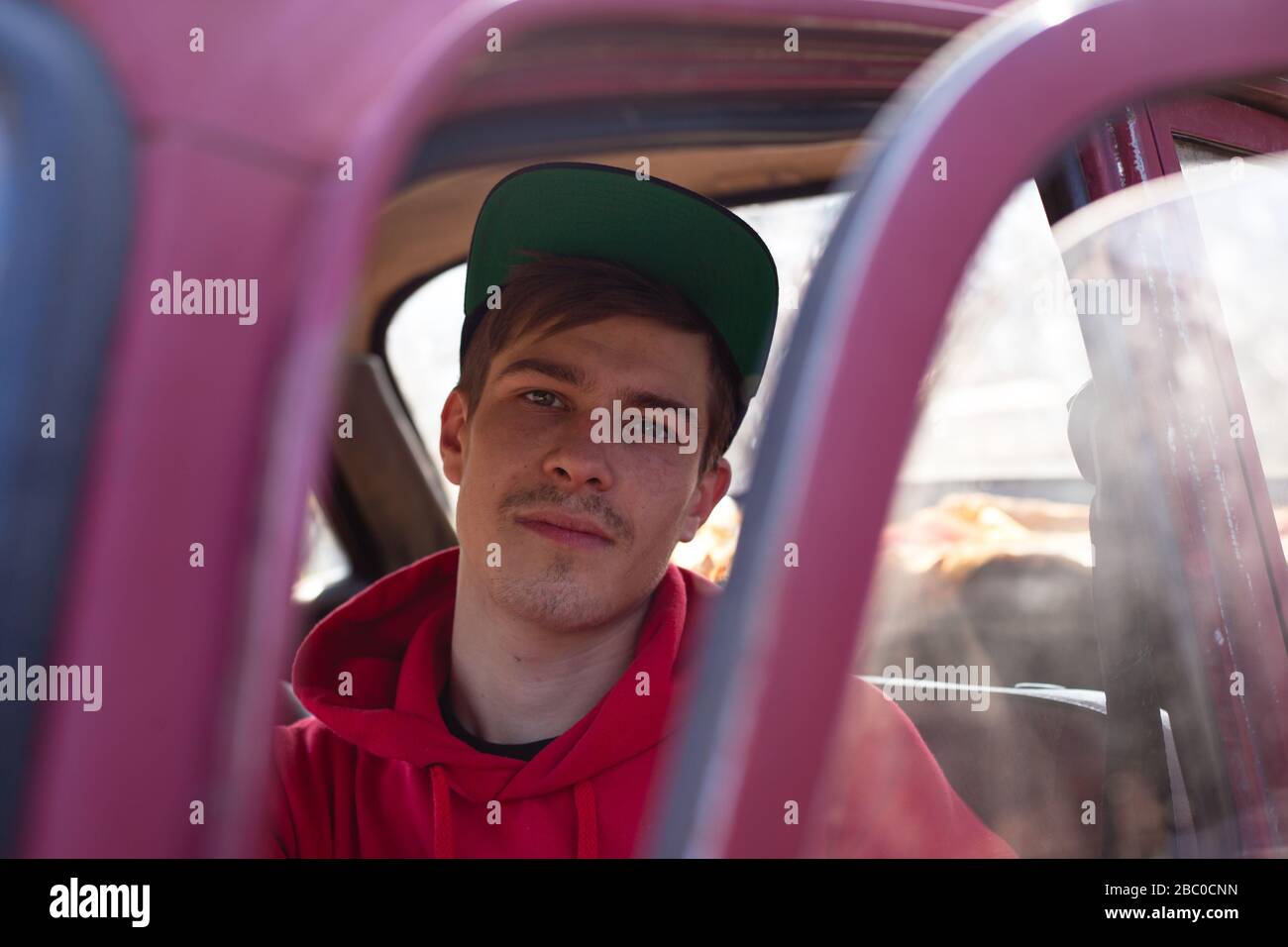 l'uomo è seduto sul sedile di guida di una vettura rossa, guardando attraverso una porta aperta. conducente stanco dopo un lungo viaggio. Foto Stock