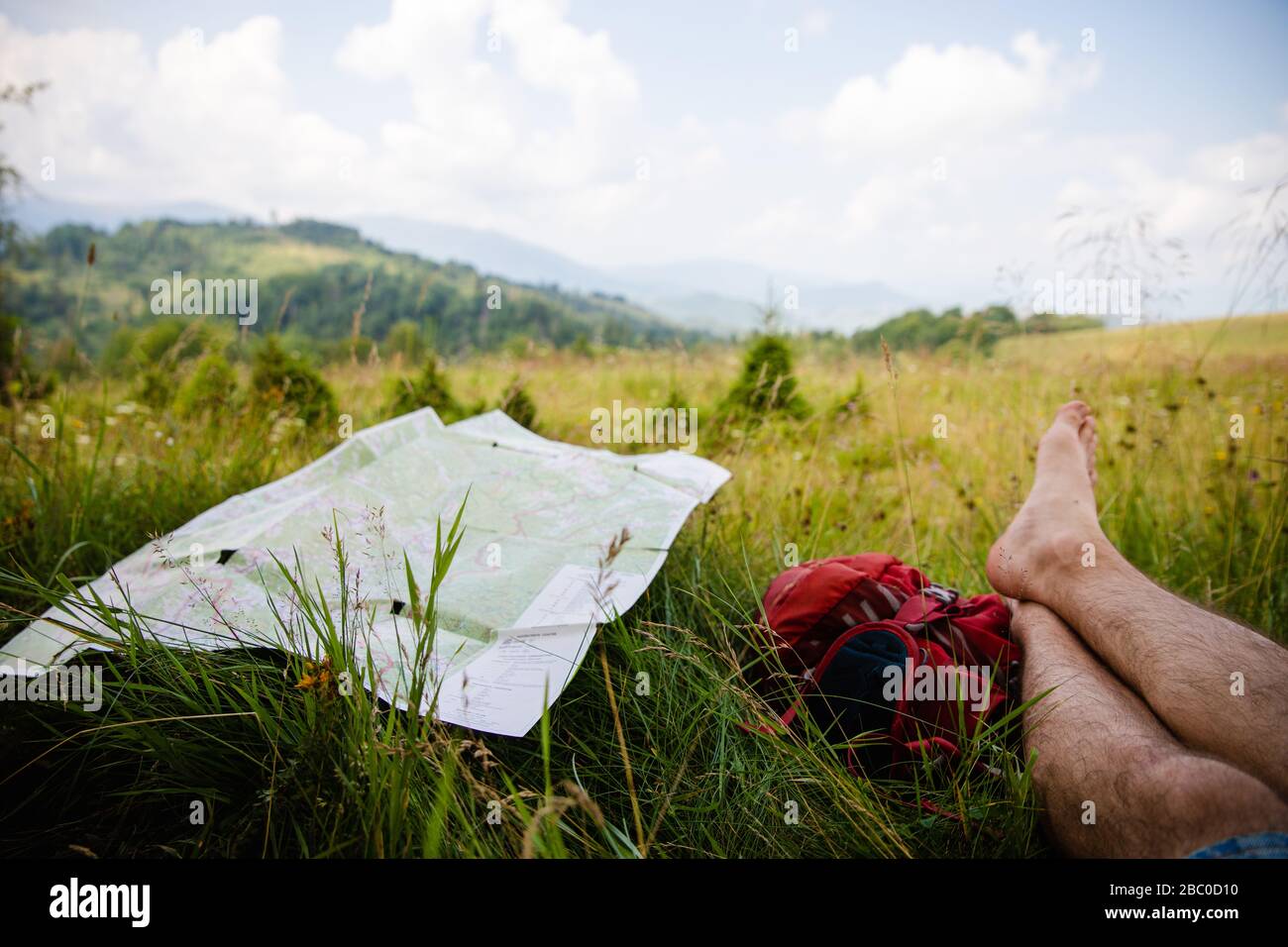 Percorsi turistici mappa su verde erba estiva vicino escursionista gambe appoggiato su zaino con belle montagne Carpazi e sfondo blu cielo Foto Stock