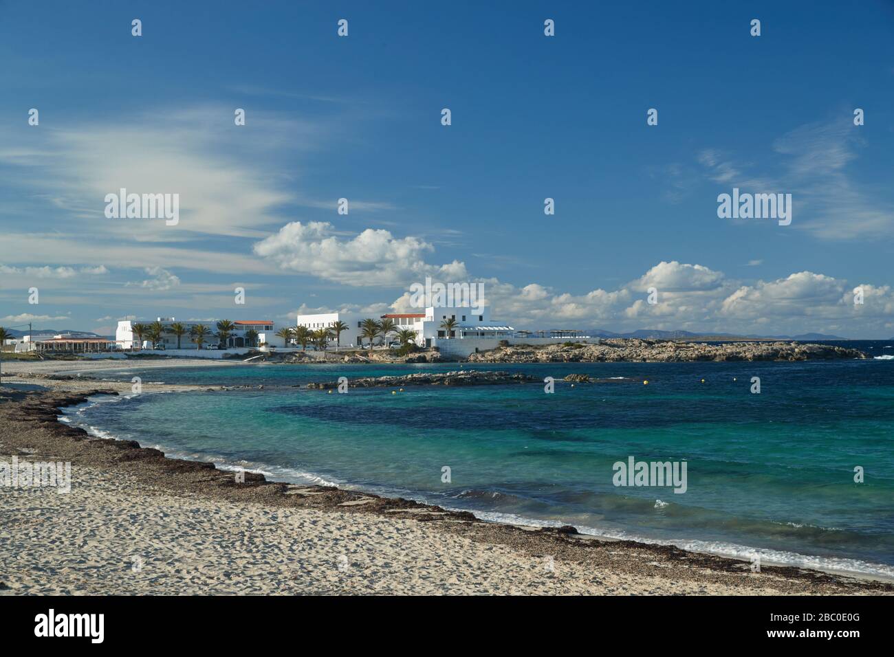 Il paesaggio del mare delle baleari e improbabile baia di bellezza, acqua azzurro, cielo con nuvole, edifici solitari è sullo sfondo, spiaggia senza persone Foto Stock