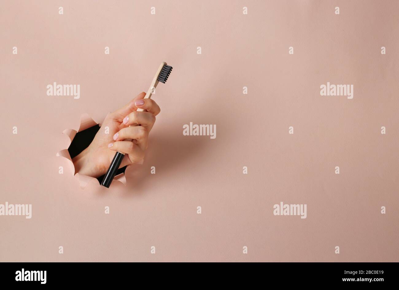 Spazzolino in legno in una mano femmina attraverso un foro rotondo in carta rosa, concetto Zero Waste, spazio di copia Foto Stock