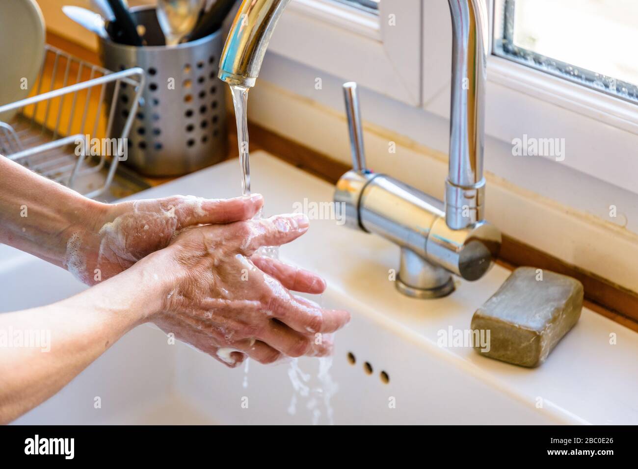 Vista ravvicinata sulle mani di una donna lavando accuratamente le mani con sapone sotto il rubinetto del lavello della cucina. Foto Stock