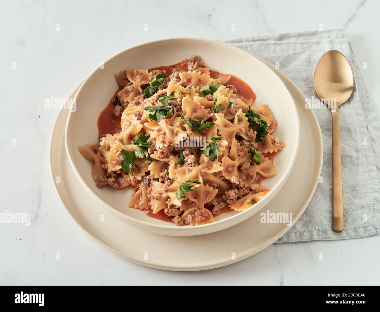 Pasta Farfalle con salsa di pomodoro e carne macinata in piatto su piano in marmo bianco. Idea e ricette per un pranzo o una cena semplice e semplice gulash di carne a una pentola. Spazio di copia Foto Stock