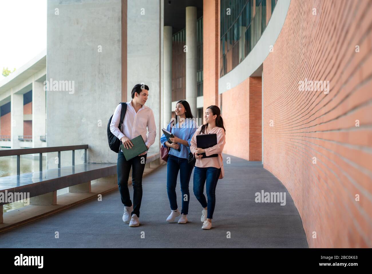 Asian tre studenti stanno camminando e parlando insieme nella sala universitaria durante la pausa in Università. Istruzione, Apprendimento, Studente, Campus, Università, Foto Stock