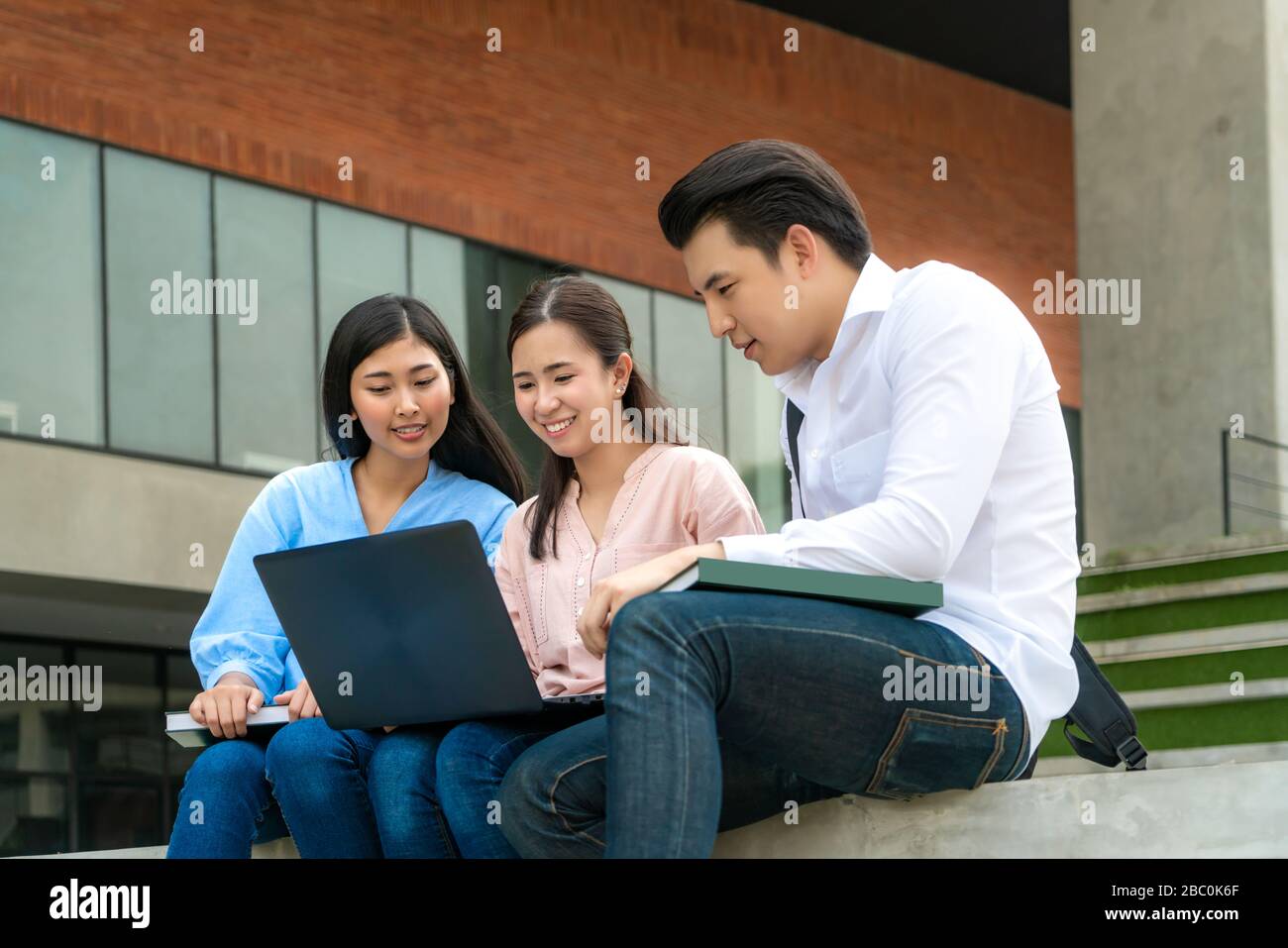 Tre studenti asiatici stanno discutendo di preparazione degli esami, presentazione, studio, studio per la preparazione dei test con il laptop dell'università. Istruzione, Lear Foto Stock