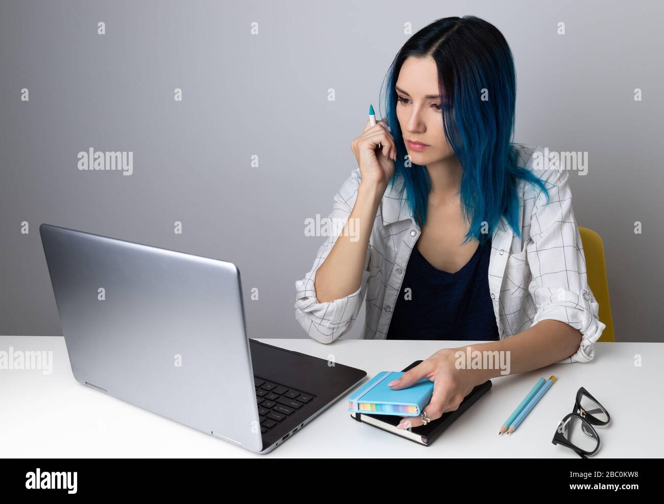 Donna hippster seria con i capelli blu che controllano le informazioni al laptop in linea Foto Stock