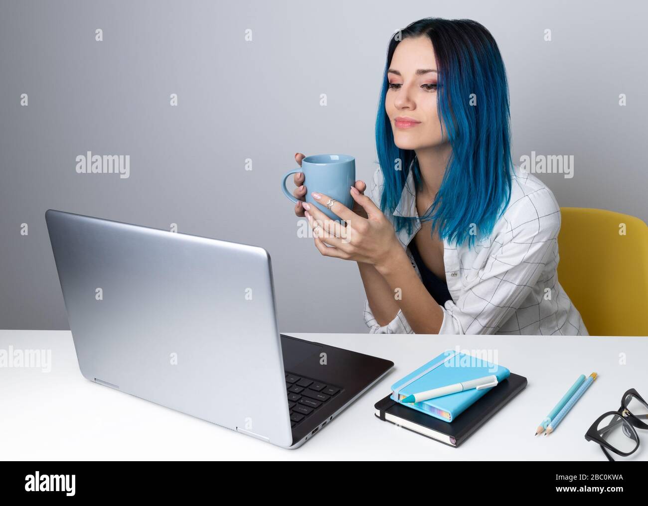 Felice giovane donna hippster con capelli blu bere caffè o tè rilassarsi con il computer portatile Foto Stock