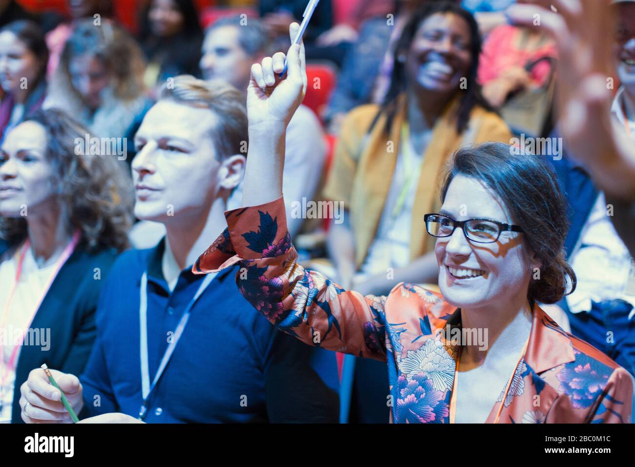 Donna sorridente nel pubblico della conferenza che alza la mano Foto Stock