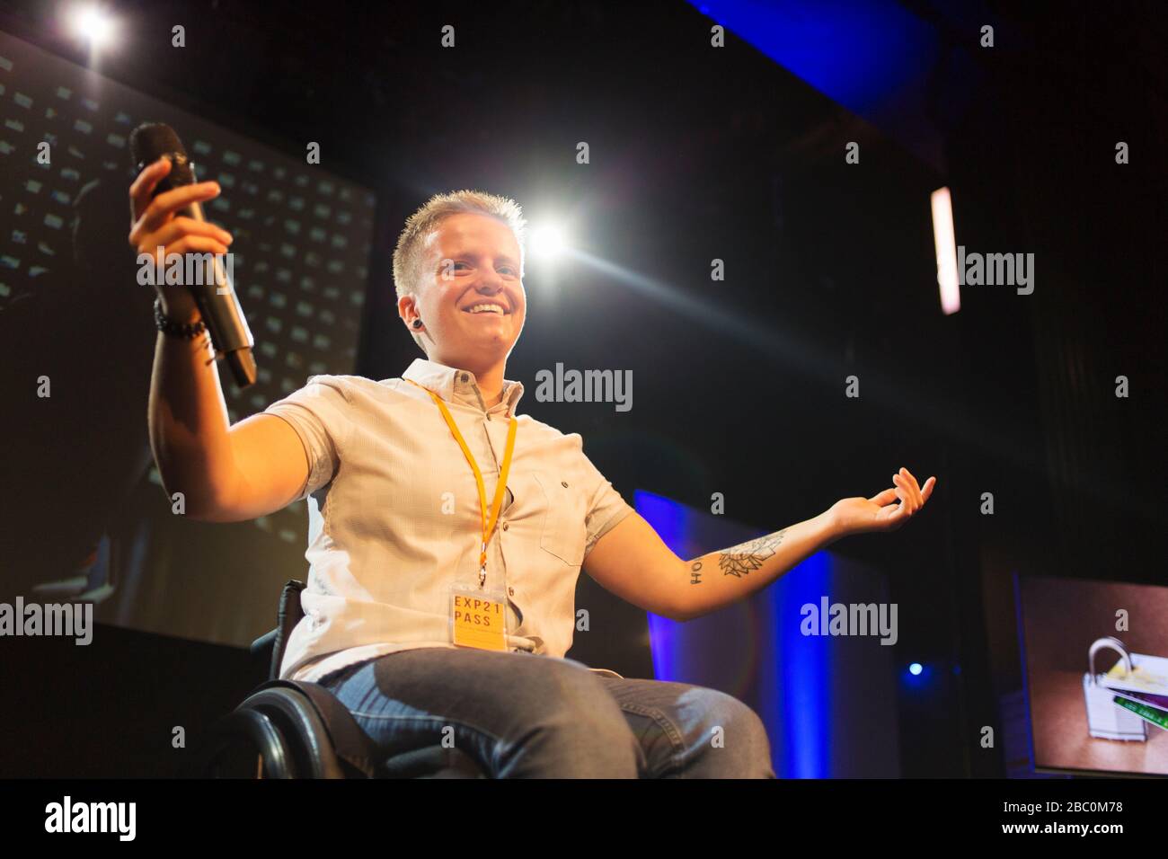 Altoparlante femmina sorridente e sicuro con microfono in sedia a rotelle sul palco Foto Stock