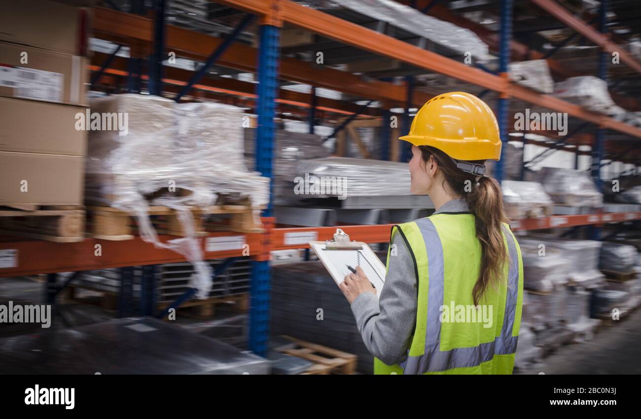 Lavoratrice di fabbrica con appunti che controllano l'inventario in magazzino Foto Stock