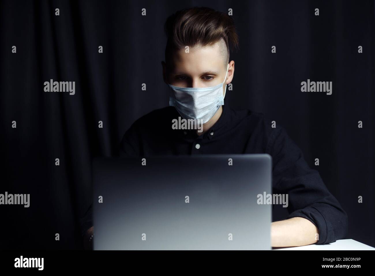 L'uomo d'affari indossa una maschera protettiva medica che lavora da casa al computer durante l'autoisolamento e la quarantena. Focolaio di coronavirus ed epidemia di covid influenzale. Spazio di copia. Foto Stock