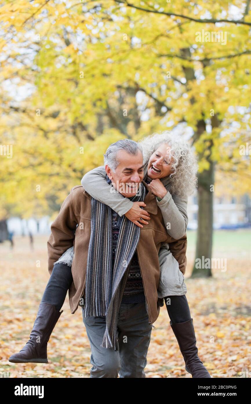 Giocosa coppia senior piggybacking nel parco autunnale Foto Stock