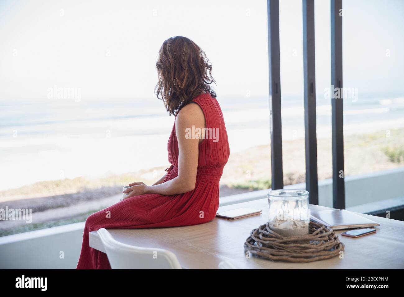 Donna bruna penosa e serena che guarda all'oceano dal tavolo della sala da pranzo Foto Stock