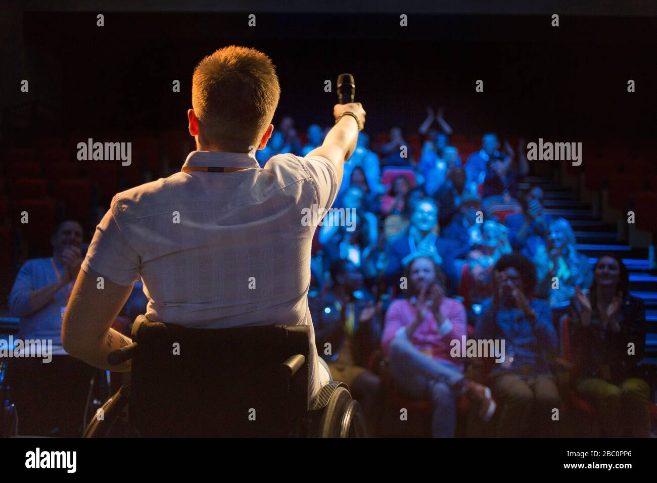 Altoparlante femmina con microfono in sedia a rotelle sul palco Foto Stock