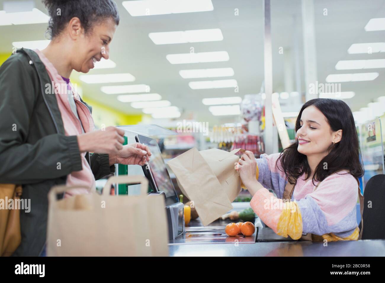 Cassa femminile che aiuta il cliente borse alimentari al supermercato checkout Foto Stock
