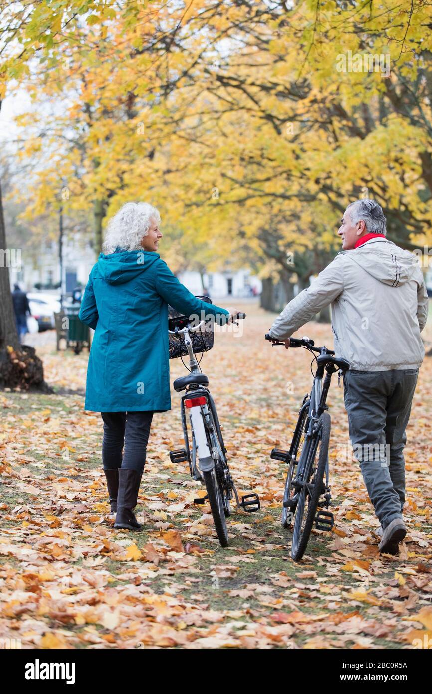 Coppia senior biciclette a piedi tra alberi e foglie nel parco autunnale Foto Stock